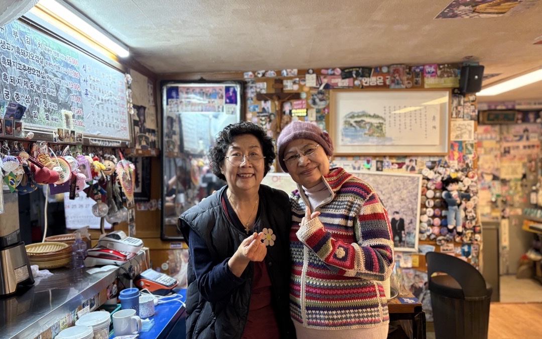An ARMY posing with the owner of a restaurant BTS frequented as trainees, both making finger hearts